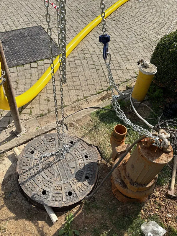 Caraskal kancasında asılı paslı drenaj pompası, yanında çıkış flanşı ve sarı spiral hortum
