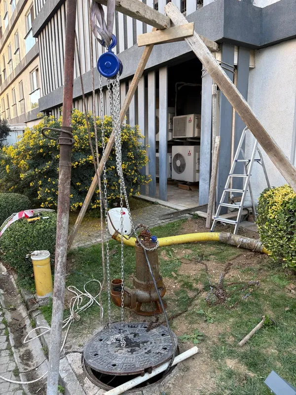 Rögar yanında üçayak ve caraskalla dışarı çıkarılmış paslı dalgıç drenaj pompası ve sarı hortum