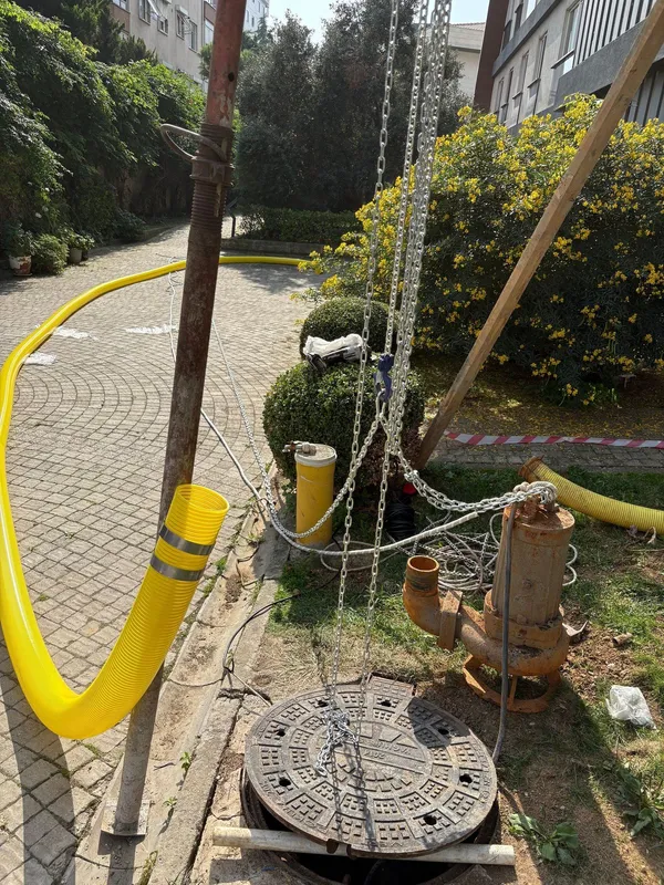 Çimde duran dalgıç pompa, çıkışında dirsek ve bağlı sarı spiral hortum